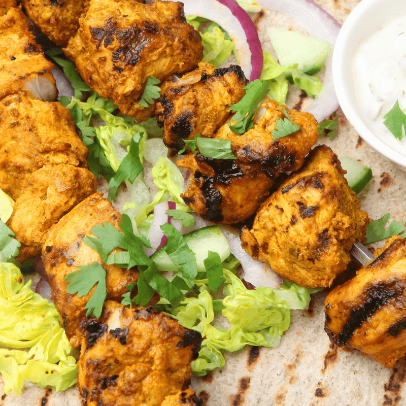 marinated chicken skewers on a flatbread with a yoghurt dip in a bowl